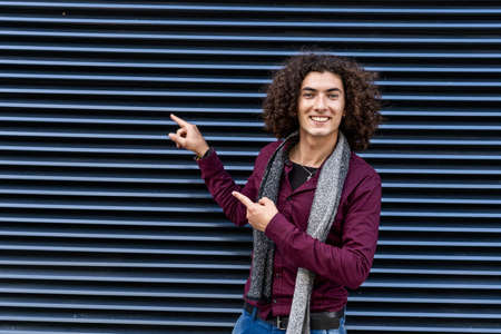 portrait of a young latin man with curly hair pointing to the side simulating a promotion on dark...