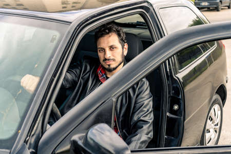 A Young Latino or Hispanic man sitting inside his car with one hand on the wheel. Concept of mobility, transportation.の写真素材