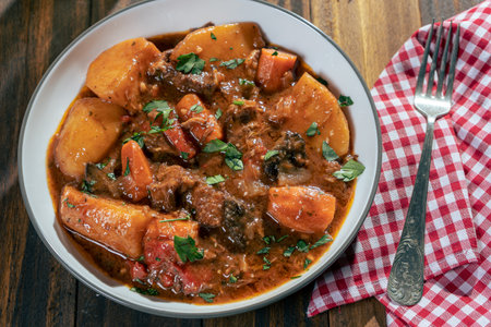 Aerial view of a plate with meat stew, potatoes and vegetables on a wooden tableの写真素材