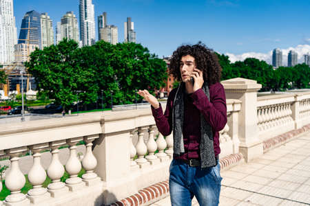 A portrait of a young curly haired latin man talking on the phone while walking down a street on a sunny day. normal viewの写真素材