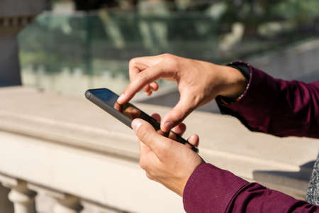 A Close-up of the hands of a man checking messages on a cell phone. Communications and technology...