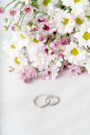 A Pair of wedding rings on a white surface with beautiful white and purple flowers in the background. Commitment and love concept. Vertical orientationの写真素材