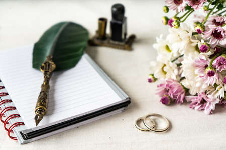 Wedding or engagement rings along with an old pen and a notepad to write a note. Beautiful flowers accompany the composition.の写真素材