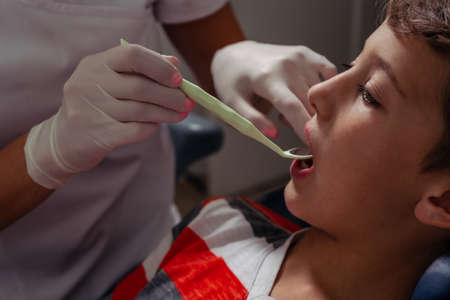 Hands of the dentist with the speculum checking the teeth of the child.
