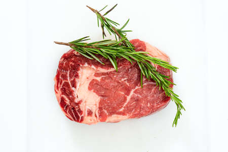 Close-up of a raw rib eye steak and a few sprigs of fresh rosemary on a white surface. Food concept. Overhead view.の写真素材