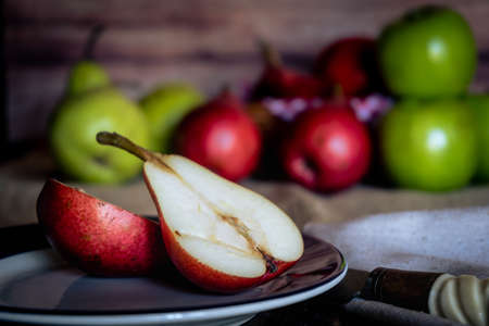 A red pear cut in half on a plate with more pears and apples out of focus in the background. Organic...