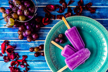 A Lollipop style grape ice cream on a stick on a vintage plate on a light blue wooden table. Concept...