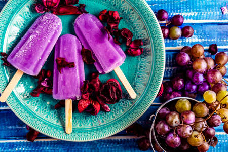 Lollipop style grape ice cream on a stick on a vintage plate on a light blue wooden table. Concept...