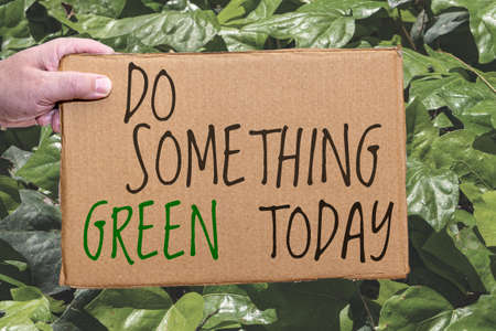 A Cardboard poster with an ecological legend on a background of leaves. Hand holds the sign from the...