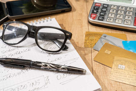 A desk surface with a notepad, pen, eyeglasses, calculator, and several credit cards. Job desk. Personal finance. Payment methods.の写真素材