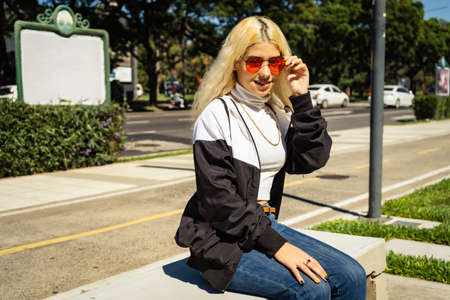 Beautiful young Latin woman in a white t-shirt sitting on a bench in a public park. Modern woman...