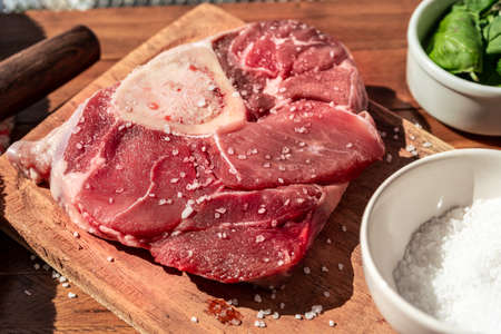 A fresh raw beef ossobuco steak on a board with garnishes on a wooden table. Animal protein concept, Italian food. aerial viewの写真素材