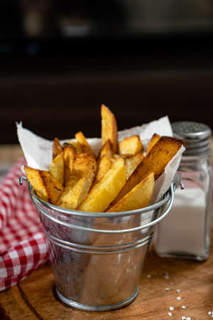 French fries in a metal pot with aioli and ketchup on a wooden board. Vertical orientation,...