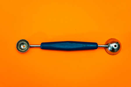 Cooking spoon to make little balls with vegetables or fruits like noisette potatoes with orange background. Kitchen and pastry utensil.の写真素材