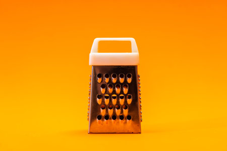 A small shiny metal grater isolated on orange background, close-up of cheese and food stainless grater.の写真素材