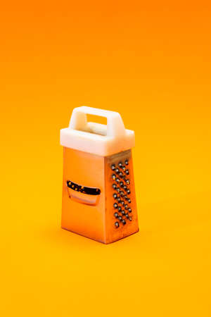 A small shiny metal grater isolated on orange background, close-up of cheese and food stainless grater.の写真素材