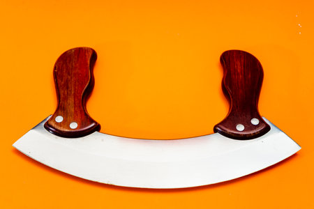 Mezzaluna knife with stainless steel blade and wooden handles insulated on orange background....