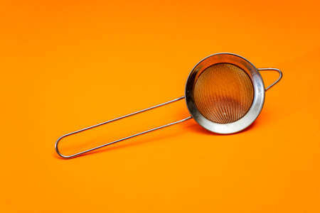 Hand strainer with fine metal mesh insulated on orange bottom.の写真素材