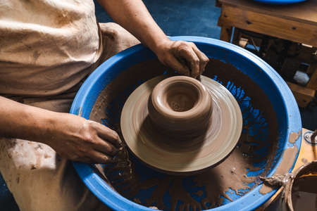 The skilled Hands of a potter working clay on a potter's wheel. The clay takes the shape the potter gives it with the terracotta tone of the clay.の写真素材