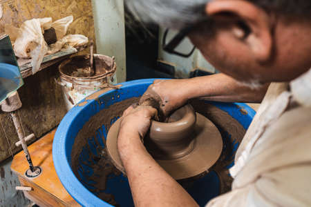 A skilled potter working the clay with his hands on a potter's wheel, shaping it as he turns. Concept of handmade craftsmanship.の写真素材
