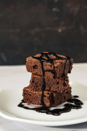 pile of chocolate brownies with strands of chocolate sauce on a white plate on a marble table. vertical orientation. Copyspace.の写真素材