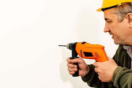 Construction Worker drilling a hole with a drill on a white wall. Copyspace.