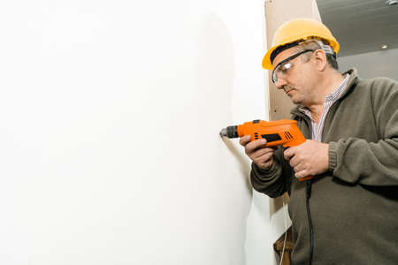 Construction Worker drilling a hole with a drill on a white wall. Copyspace.