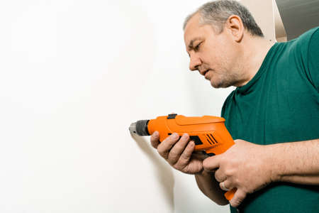 Construction Worker drilling a hole with a drill on a white wall. Copyspace.
