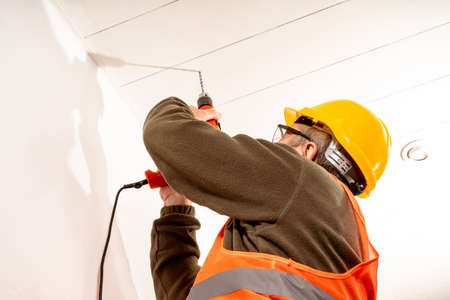 Operator dressed in safety uniform like vest, helmet and safety glasses, drilling a roof with a...