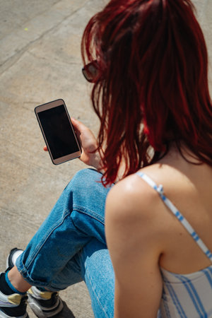 Beautiful latin woman with red hair looking at her cell phone. Copyspace. Portraitorientation.の写真素材