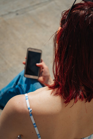 Beautiful latin woman with red hair looking at her cell phone. Copyspace. Portraitorientation.の写真素材