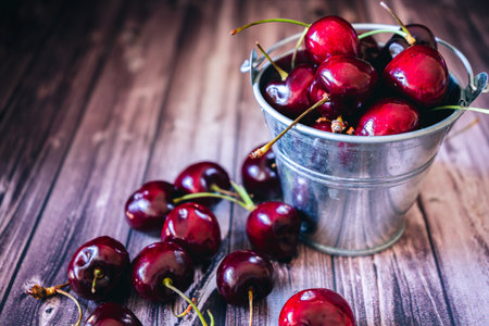 A Cherries in a brass bucket on a wooden table. Space for text. Dark food style.