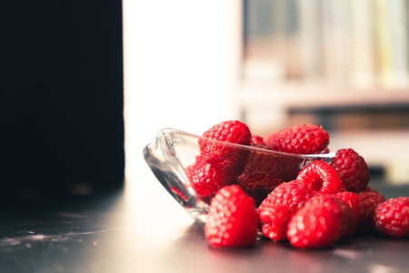 Normal view of a Serving of Raspberries in a small clear bowl on a black granite surface and backlit...