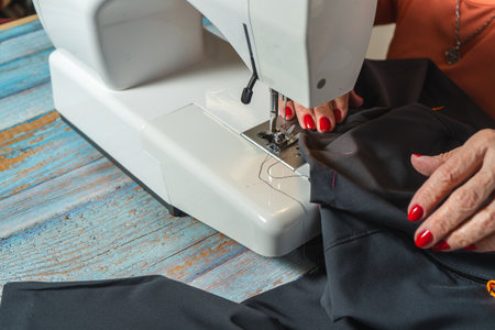 Hands of a female seamstress sewing a pair of pants on a sewing machine.