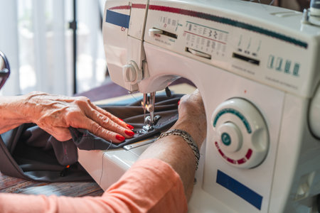Hands of an old female seamstress sewing a pair of pants on a sewing machine.の写真素材