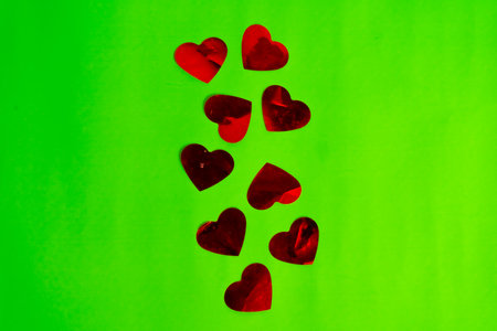 Red hearts made of metallic paper on a green surface. Ideal for use in graphic compositions.の写真素材