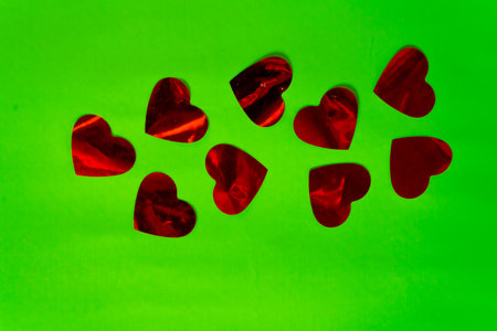 Red hearts made of metallic paper on a green surface.の写真素材