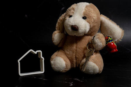 Profile of miniature family house next to keys on a key ring held by a stuffed dog. Concept of new family home.の写真素材