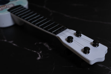 Frets and headstock of a toy ukulele with childish colors on a dark background. Music concept.の写真素材