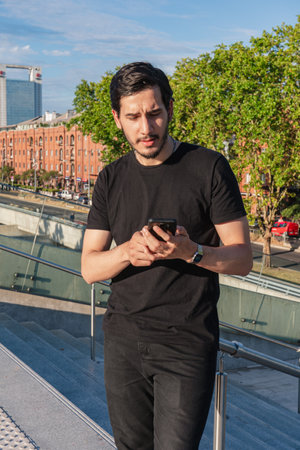 Young man standing smiling relaxed and calm checking and answering his smartphone messages