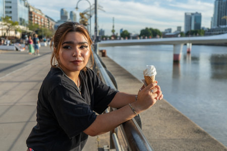 Young woman enjoys an ice cream cone by the river in Puerto Madero, Buenos Aires, on a sunny dayの写真素材