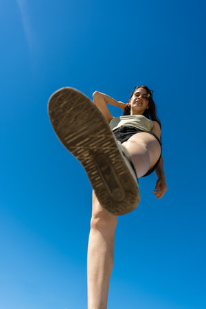 Low angle view of elegant young latin woman taking a step forward against blue sky