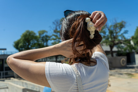 Elegant latin woman arranging her hair decorated with flower ornament on a sunny day, enjoying the warm weatherの写真素材