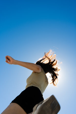 Carefree young latin woman enjoying a sunny day, walking towards the sun with blue sky background,...