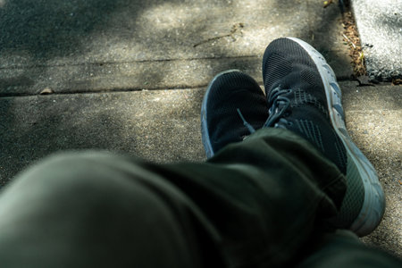 Pov shot of a man resting with his feet up on a concrete surface, wearing black sneakers and green pantsの写真素材