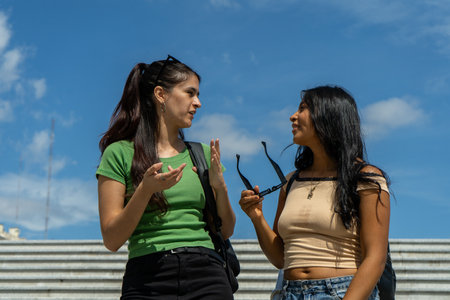 Two female students are discussing on campus on a sunny dayの写真素材