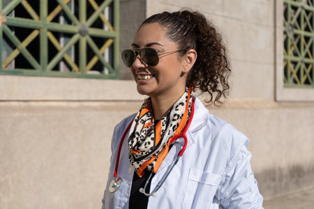 Female medical professional wearing sunglasses and a fashionable scarf outside a hospital building