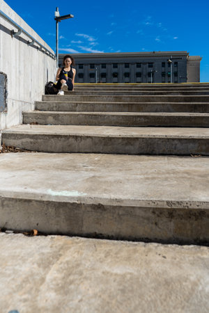 Sportswoman taking a break on concrete steps in the city, enjoying a refreshing drinkの写真素材