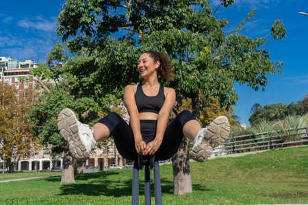 Happy sportswoman strengthening her abdominal muscles using outdoor gym equipment in a park
