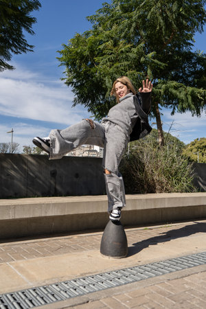 Young woman showcasing her balancing skills on a bollard in a park, expressing urban style and...